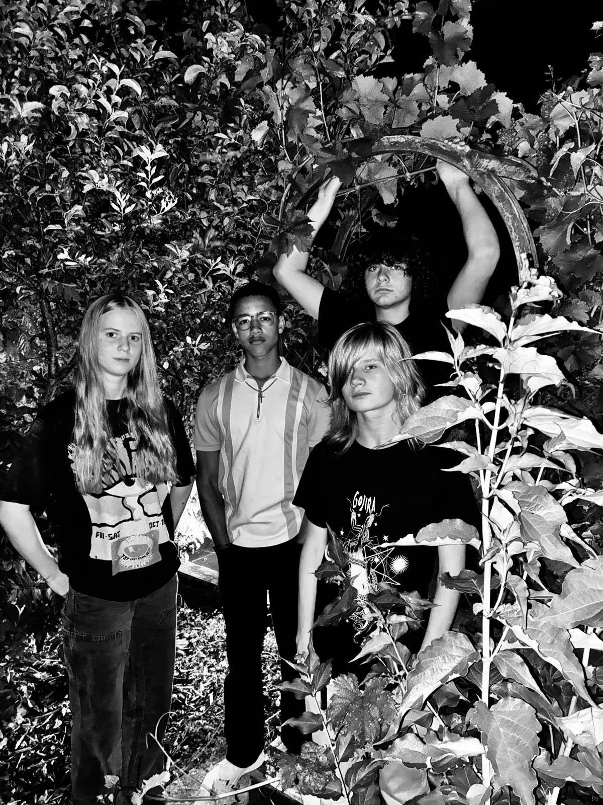 The four members of Unførgiven photographed at night against a hedge, lit hard by a camera flash.